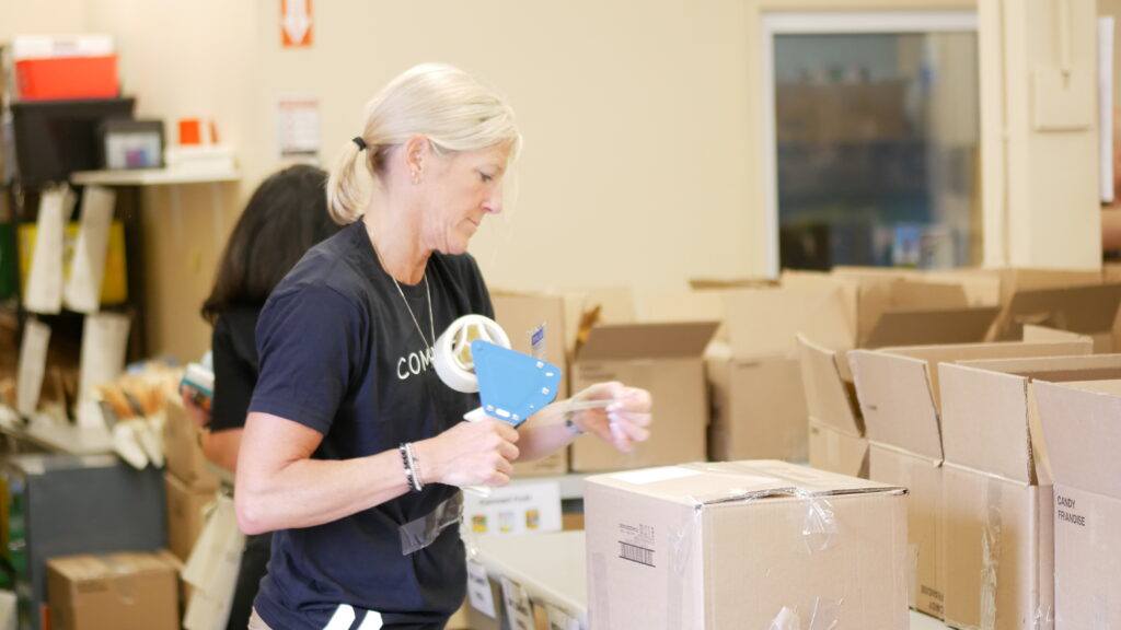 Movati Athletic team member taping a filled box of non-perishable food.