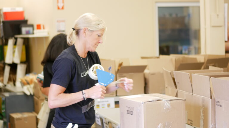 Movati Athletic team member taping a filled box of non-perishable food.