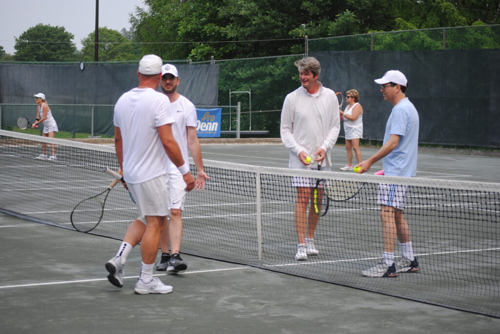 Four men gathered around a tennis net having a conversation.