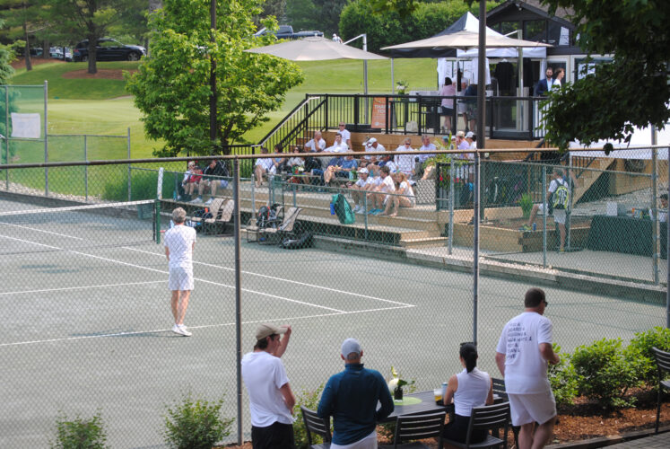 A panoramic photo of a tennis court with people sitting in the stands.