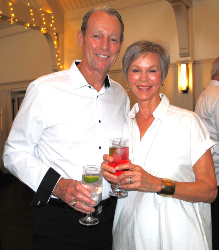A man and woman standing side by side holding drinks and smiling at the camera.