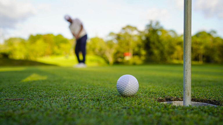 Golfer putting ball on the green golf, lens flare on sun set evening time. Golfer action to win after long putting golf ball in to the hole.