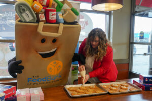 CEO Kim Wilhelm decorating Holiday Smile Cookies with The Food Bank’s mascot, Phil the Food Drive Bag.